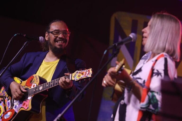 Muzycy grający na gitarach na scenie koncertowej.