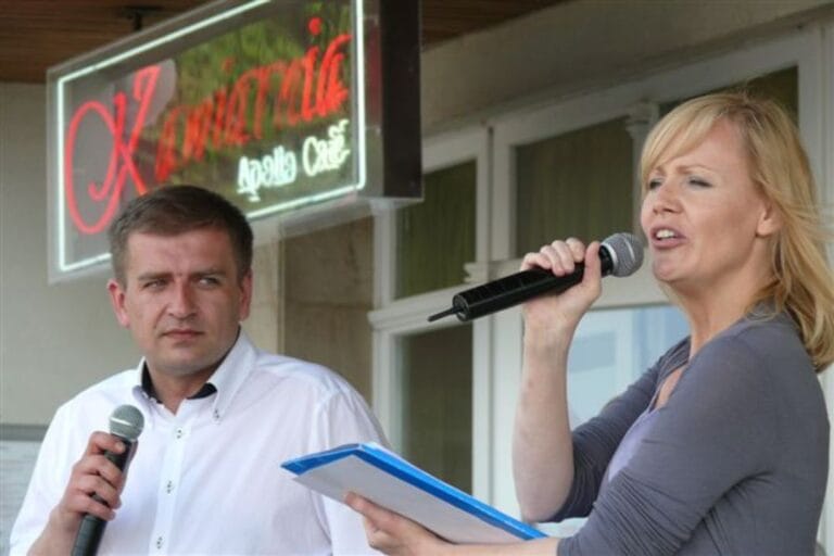 Dwie osoby z mikrofonami przed kawiarnią.