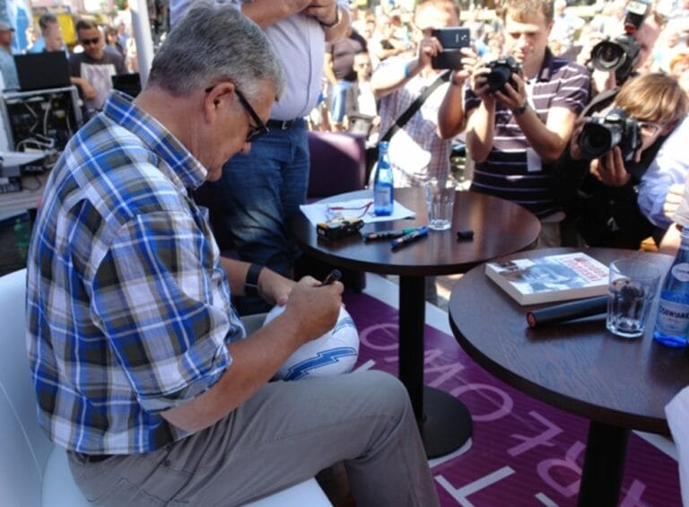 Mężczyzna podpisuje piłkę na spotkaniu z mediami.