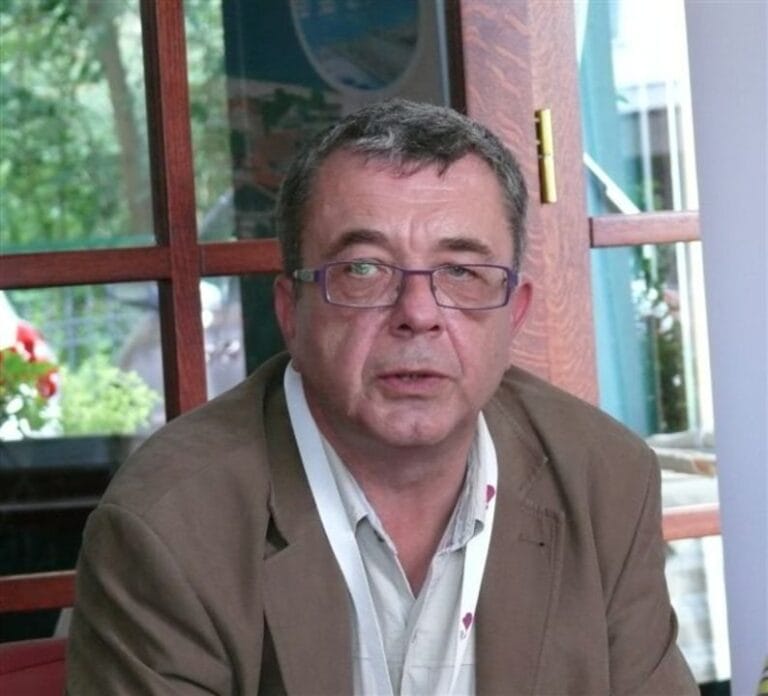 Mężczyzna w okularach i marynarce siedzi przy oknie.