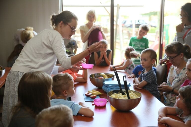 Dzieci uczą się gotować z dorosłymi przy stole.