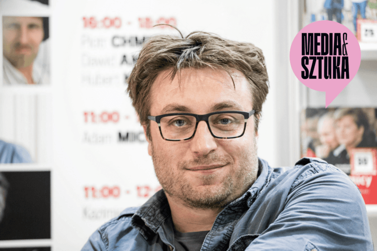 Mężczyzna w okularach na tle plakatu.