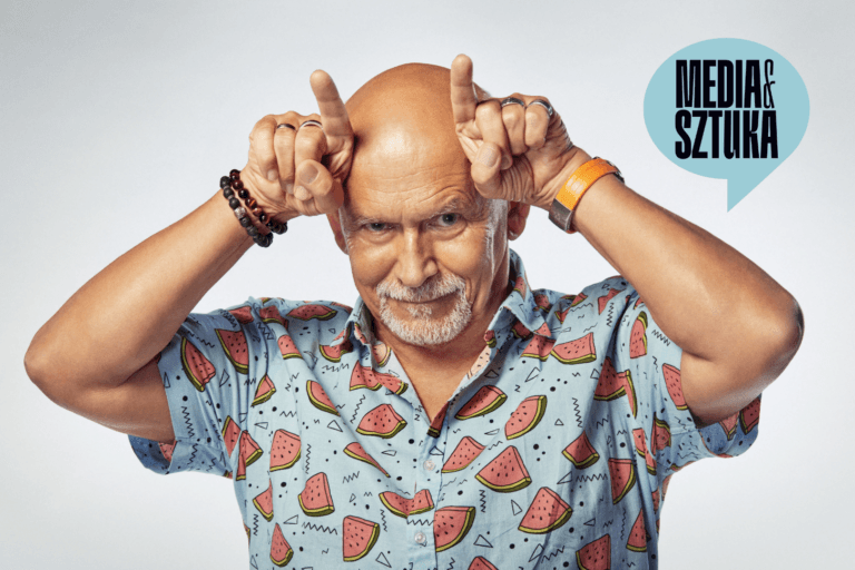 Uśmiechnięty mężczyzna w kolorowej koszuli, robi znak rogów.