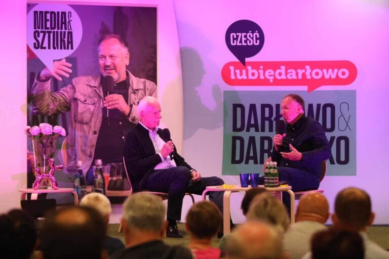 Dyskusja dwóch mężczyzn na scenie z mikrofonami.