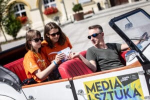 Trójka osób w otwartym samochodzie na festiwalu.