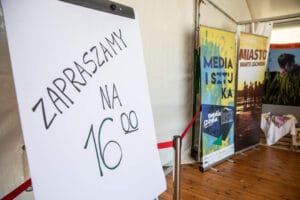 Plakat zaprasza na 16:00 obok banerów promocyjnych.