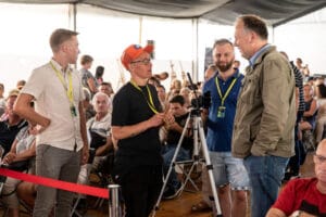 Grupa ludzi rozmawia na wydarzeniu w namiocie.