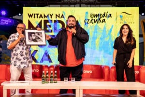 Trzech ludzi na scenie trzymających mikrofony.