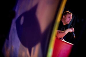 Osoba z mikrofonem na scenie, cień na kurtynie.