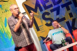 Mężczyźni na konferencji, mikrofony, baner reklamowy.