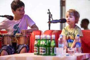 Dzieci z bębnami na scenie, mikrofony i napoje.