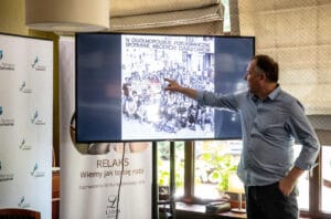 Mężczyzna wskazuje na zdjęcie grupowe na ekranie.