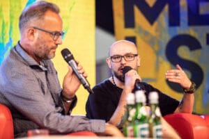 Dwóch mężczyzn rozmawia na scenie z mikrofonami.