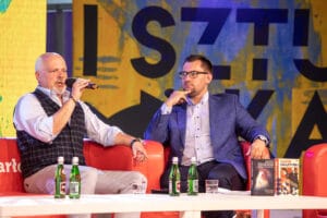 Dwaj mężczyźni na scenie z książkami i mikrofonami.