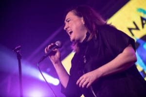 Kobieta śpiewa na scenie z mikrofonem.