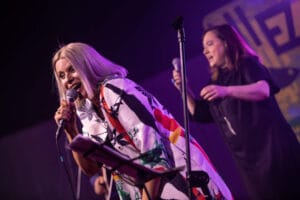 Wokalistki występujące na koncercie, mikrofony w dłoniach.