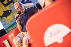 Mężczyzna z mikrofonem na scenie, kolorowe tło.