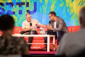 Dyskusja dwóch mężczyzn na czerwonej kanapie z mikrofonami.