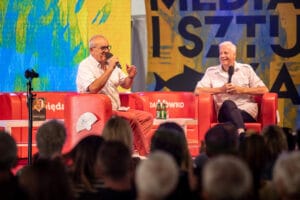 Dwóch mężczyzn siedzi i rozmawia na scenie.